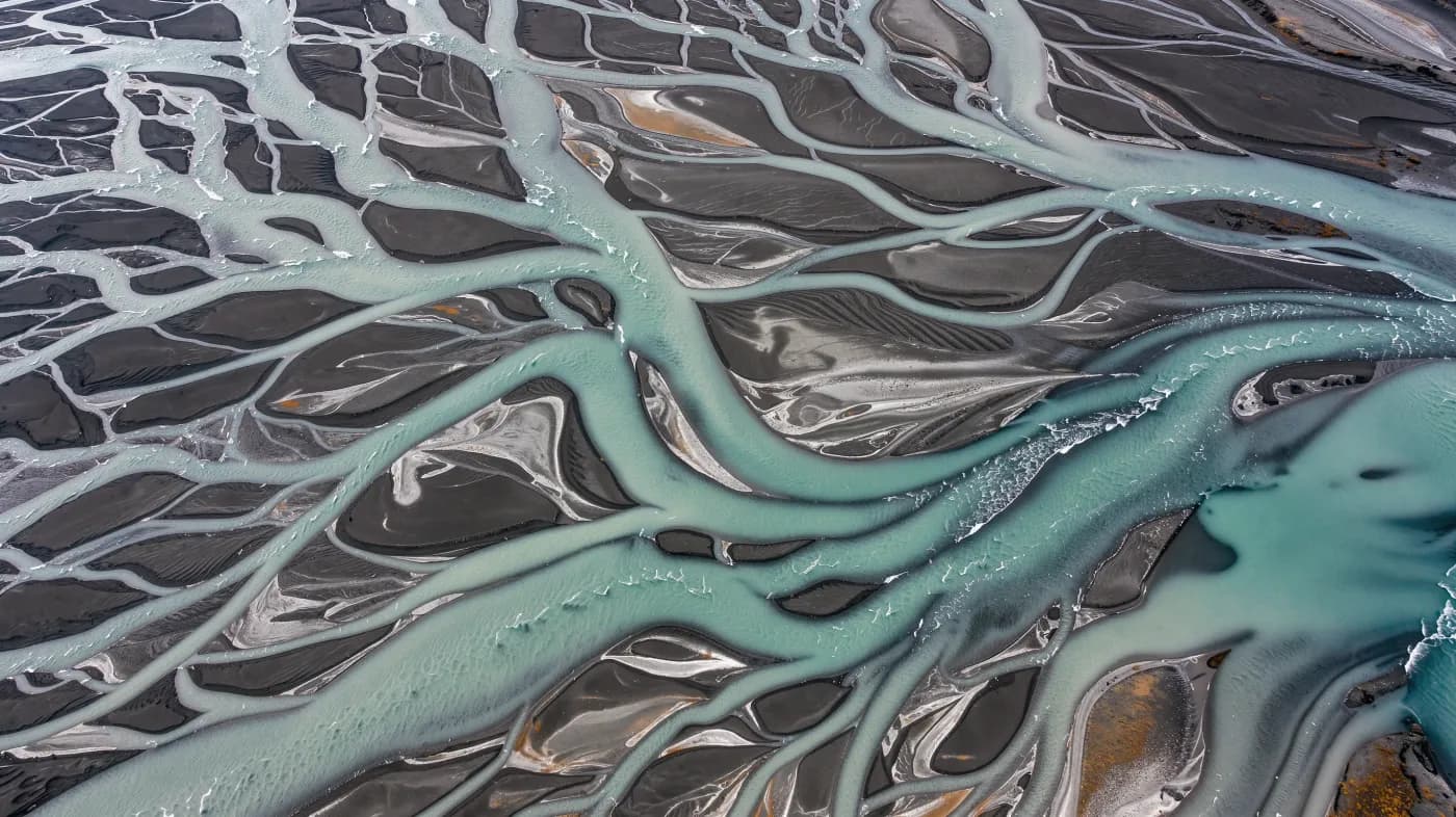 Aerial photograph of braided glacial rivers in Iceland, turquoise water and charcoal black sand, abstract patterns